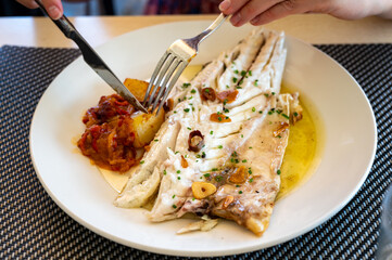 Eating in restaurant of fresh grilled on old charcoal parrillas sea bass fish in small fisherman's village Getaria, Basque Country, Spain
