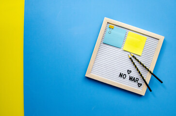 Flatlay horizontal composition empty letter board with the words No War, pray for Ukraine, patriotic colors blue and yellow sticker, black pencils, empty blue background