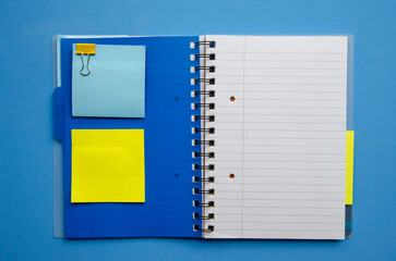 Flatlay empty space dark blue cover notebook spring with blank pages strip, blank stickers blue and yellow, central composition
