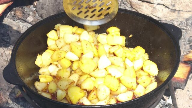 The cook stirs the potatoes in oil. Dishes of the national cuisine of the peoples of Asia. Vegetables and meat are cooked in a cauldron. 