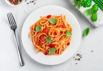 Italian pasta with tomatoes and basil on a light gray background. Top view, close-up.