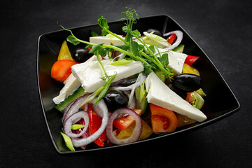 Greek salad with cheese and vegetables, on a black plate
