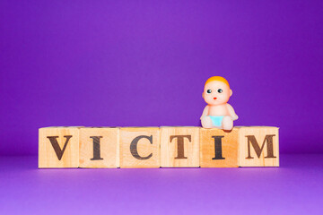 Naklejka premium text the word victim from wooden letters,on the letter sits a miniature toy newborn.Purple,veri peri background,copy space.