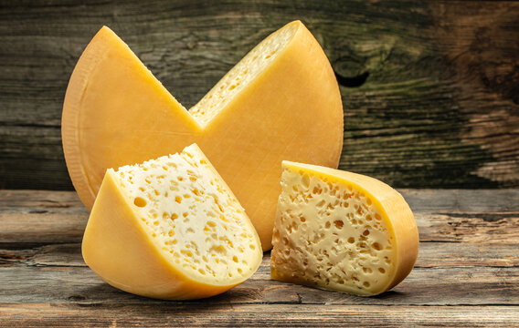 Cheese wheel with cut a piece of cheese triangular shape from a large cheese head. cheese maasdam with big holes on a wooden background
