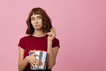 Excited confused cute redhead lady in red t-shirt with popcorn ready for movie evening posing isolated on over pink studio background. Copy space Banner. Fashion Cinema concept. Entertainment offer