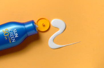 Blue Plastic bottle of sun protection and squeezed white cream texture on orange background.