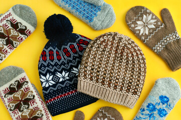Hats and mittens on a yellow background. Clothing in the form of hats and mittens for cold seasons. Knitted hats and warm mittens are seen from above.