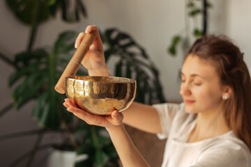 Young woman playing on a singing tibetian bowl.Relaxation and meditation.Sound therapy,alternative medicine.Buddhist healing practices.Clearing the space of negative energy.Selective focus,close up.