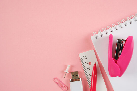 Notepad,pen,ruler,stapler,USB flash drive,paper clips in pink and white tones on a pink background.Goods for businessmen,schoolchildren, students,teachers.Planning,office work,sale of office supplies