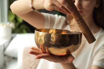 Young woman playing on a singing tibetian bowl.Relaxation and meditation.Sound therapy,alternative medicine.Buddhist healing practices.Clearing the space of negative energy.Selective focus,close up.