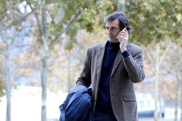 Smiling senior man, businessman talking on the phone while walking around the city,