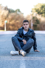 young happy boy teenager sitting on asphalt road in front of the camera in posed portrait