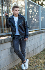 young happy boy teenager leaning on a metallic fence, looking away