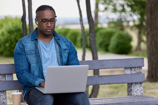 Focused African man nervously awaits an important email from a business partner. Black guy sits on a bench with a laptop waiting for a suitable job. Entrepreneur works remotely