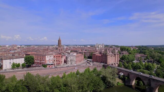 drone aerial view of Montauban in the south of france with a bridge, red stone buildings, greenery and beautiful churches visible. Cars drive freely in front of the town and on the bridge