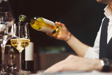 Bartender pouring sparkling white wine into wineglasses.