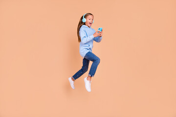 Fototapeta na wymiar Full length photo of beautiful excited schoolgirl run jump use telephone media app isolated on beige color background