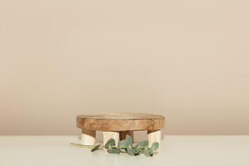 Empty round wooden podium for product presentation and eucalyptus leaves on beige background for...