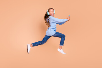Fototapeta na wymiar Full length profile portrait of carefree excited girl jump rush fast use hold telephone isolated on beige color background