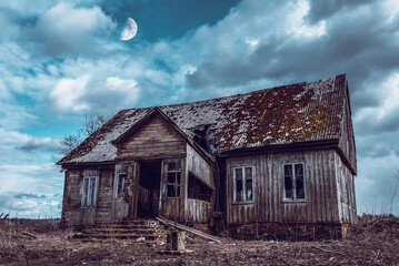Obraz premium Old neglected wooden house,dramatic clouds at night. Abandoned Haunted Horror House.Darkness with a moon.Toned.