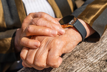 Elderly woman with smart watch fitness band checking her pulse,outdoors on the old wooden table,sumer sunny day. closeup.