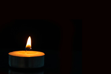 Image of an orange coloured tea candle set against a jet black background. Idea for advertising, wallpaper for banner use.