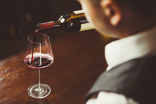 Close-up photo, sommelier pours red wine to glass on bar counter background.