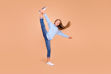 Full body portrait of excited cheerful girl hand hold one split leg stretching isolated on beige...