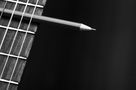 Black and white image of a classical acoustic guitar with a pencil.
