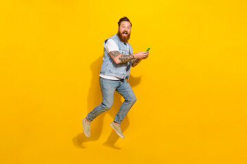 Fototapeta na wymiar Full body photo of overjoyed sporty man hold telephone jumping isolated on yellow color background