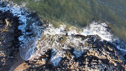 Aerial view looking  straight down onto waves crashing onto rocks. 