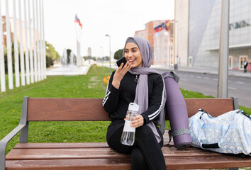 Muslim woman, sitting on a bench, looking at her smartphone - woman in sportswear -