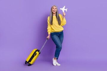 Photo of adorable excited retired woman wear sweater holding suitcase aircraft isolated violet color background