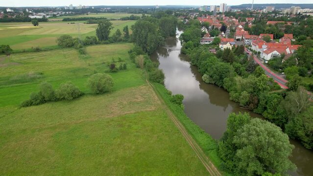 The drone flies over a rural landscape over the river Regnitz and the suburb of Erlangen-Bruck

