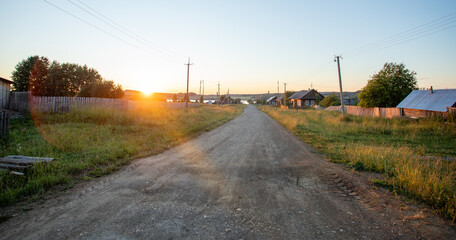 Fototapeta na wymiar Sun-drenched ground road leading to river in village at sundown in Russia.