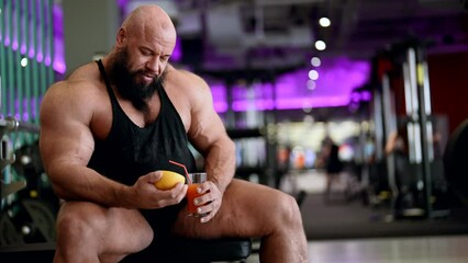 professional sportsman is drinking grapefruit juice in gym after training, muscular powerlifter