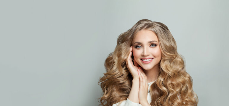 Closeup of happy pretty blonde young woman with long wavy hair smiling against white studio wall banner background