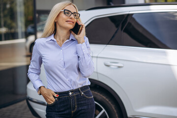 Aged business woman talking on the phone by the car