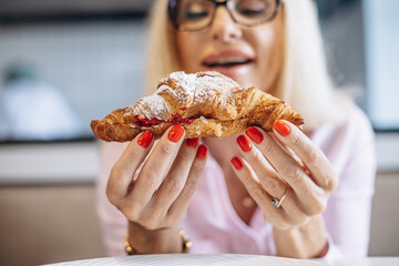 Aged woman eating delicious croissant in a cafe