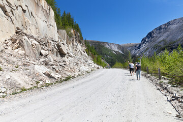 Group of tourists walk along a mountain road on a sunny day. Travel, walks in nature and hiking in the mountains. The concept of active recreation. Nuhu pass, Mondy-Orlik road, Buryatia - obrazy, fototapety, plakaty