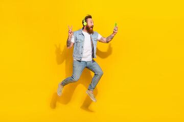 Full size photo of active excited man jump hold phone take selfie show v-sign isolated on yellow color background