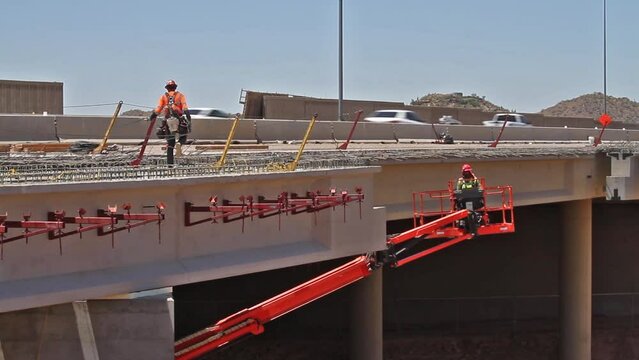 Freeway bridge under lane addition construction with traffic and worker on deck, worker in snorkel lift.
