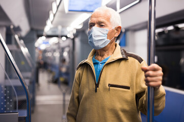 Old man in face mask standing in subway car