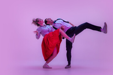 Emotional expressive young man and pretty woman in vintage style outfits dancing retro dance isolated on very peri color background in neon light.