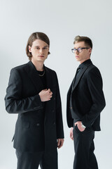 Young gay couple in formal wear looking at camera isolated on grey.