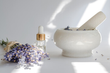 Transparent bottle with lavender oil, mortar and pestle and fresh lavender flowers