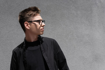 Obraz premium Young man in eyeglasses and black clothes looking away on urban street.