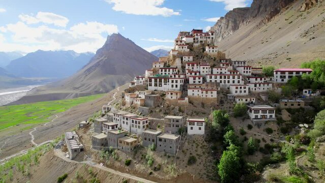 Aerial Drone moving wide shot of a Kee Gompa or Key Monastery over a peak of mountain with a beautiful landscape view of hilly region against clear blue sky in a daylight Spiti valley, India.