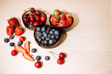 Fruits, blueberries, strawberries, cherries, in round glass plates on a beige table. View from above
