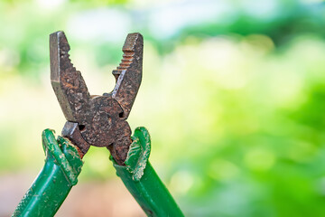 Fototapeta premium Rusty pliers. Old rusty pliers are open on a blurred natural background. Old working tool. Close up image. Selective focus.